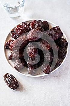 Medjoul dates in a white plate and glass of water on a gray background