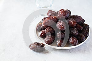 Medjoul dates in a white plate and glass of water on a gray background. Close up