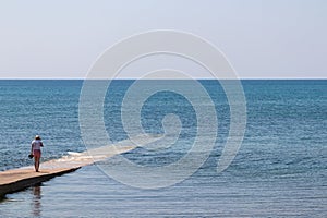 Medulin - Tourist woman walking on concrete pier in the waters of Adriatic Sea in coastal town Medulin, Istria peninsula, Croatia