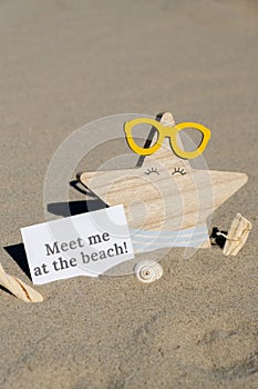 MEET ME AT THE BEACH text on paper greeting card on background of funny starfish in glasses summer vacation decor. Sandy