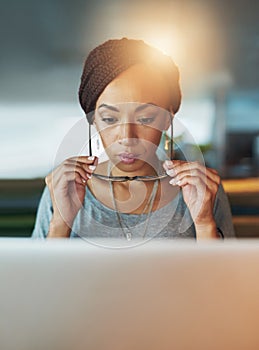 Meeting deadlines is what she does. a young woman using her laptop while working late in her office.