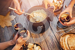 Meeting of friends, girl is cooking Swiss fondue assorted cheeses dinner on fire, hands holding mulled wine background