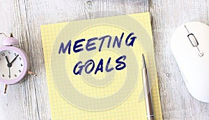 MEETING GOALS text written in a notebook lying on a wooden work table