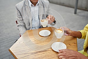 Meeting with a good friend. Cropped photo of stylish people drinking coffee in a cafe outdoors