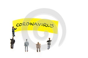 Meeting with miniature figurines posed as business people standing around post-it note with Coronavirus handwritten message in