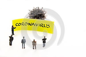 Meeting with miniature figurines posed as business people standing around post-it note with Coronavirus handwritten message in