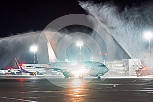 Meeting a new aircraft at a night airport, the tradition of wash spray pouring water from fire trucks.