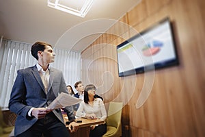 Meeting of office workers at the table, looking at the presentation with diagrams on the TV