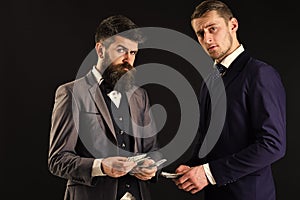 Meeting of reputable businessmen, black background. Man with beard on serious face counting money, pay to partner