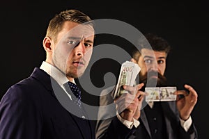 Meeting of reputable businessmen, black background. Man on serious face hold roll made out of dollar, money, pay to