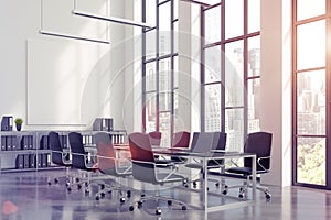 Meeting room interior with a long black table with laptops standing on it and a vertical poster on a white wall.