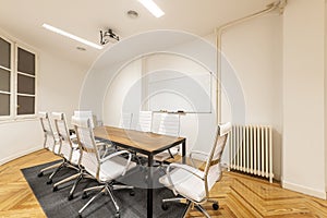 Meeting room with wooden office table with metal frame and swivel chairs upholstered in white skai, whiteboard for erasable