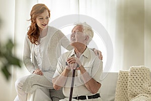 Meeting of smiling granddaughter with happy grandfather with walking stick at home