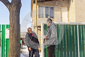 Meeting of two mature neighbors at the gate of a rural house