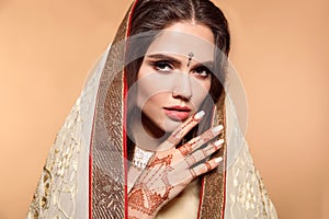 Mehendi. Portrait of beautiful indian girl in saree isolated on beige. Young hindu woman model with kundan golden jewelry set.