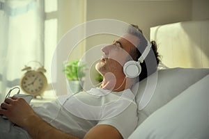 Melancholic adult man listening to music lying in bed detail