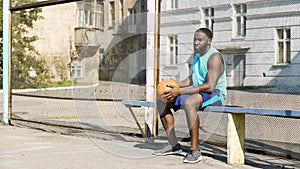 Melancholic Afro-American male sitting on bench and playing ball, loneliness