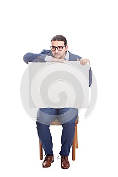 Melancholic businessman seated on chair holding a big blank banner with copy space for messages. Full length business person