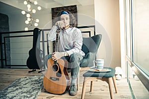 Melancholic handsome musician showing acoustic guitar while holding it