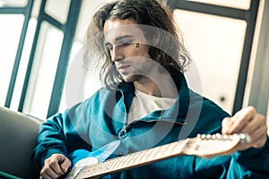 Melancholic long-haired young musician with small tattoo checking strings
