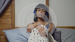 Melancholic woman in headphones sitting on bed