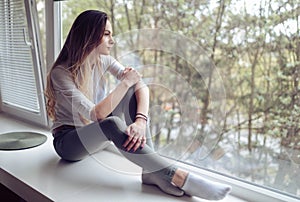 Melancholic woman sitting on window ledge at home