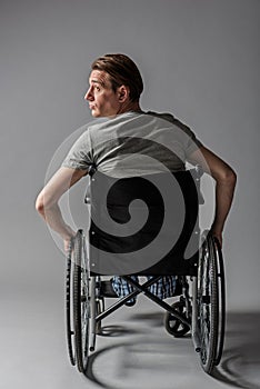 Melancholy disabled young man taking seat in special armchair