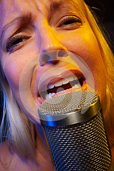 Melancholy female vocalist under gelled lighting sings with passion into condenser microphone