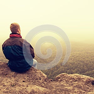 Melancholy and sad day. Man at enge of rock above deep vally. Tourist on the peak of sandstone rock watching to mist.