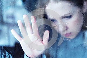 Melancholy and sad girl at the window in the rain photo