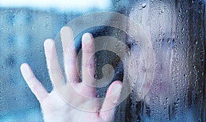 Melancholy and sad young woman at the window in the rain