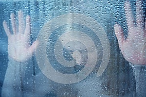 Melancholy and sad young woman at the window in the rain