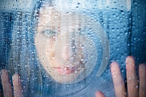 Melancholy and sad young woman at the window in the rain photo