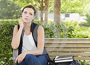 Melancholy Young Adult Woman Sitting on Bench Next to Books photo