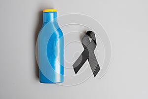 Melanoma and skin cancer awareness month. black Ribbon and body sunscreen bottle on grey background. World cancer day concept