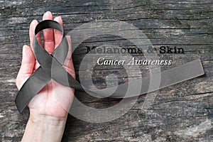 Melanoma and skin cancer black awareness ribbon on human helping hand old aged background photo