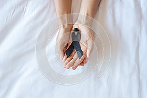 Melanoma and skin cancer, Vaccine injury awareness month and rest in peace concepts. Man holding black Ribbon on white bed