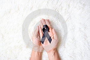 Melanoma and skin cancer, Vaccine injury awareness month and rest in peace concepts. Man holding black Ribbon on white bed