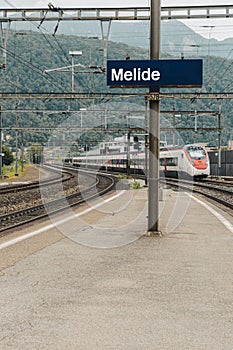 Melide station, blue sign with the name of the station. The high speed train is coming
