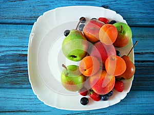 Mellow fresh summer fruits and berries mix in white plate on green wooden background with copy sapce, strawberries, blueberries,
