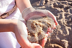 Mellow heart shaping female hands above beach