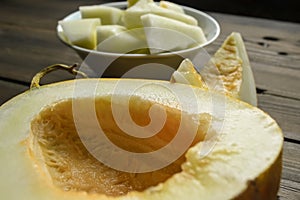 Melon close-up on a wooden table. In the background are pieces of melon in a plate and one slice. Ripe melon - slicing.