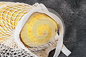 melon in a cotton net. Mesh shopping bag with Torpedo melon. Ripe juicy melon in a cotton mesh bag on a marble dark