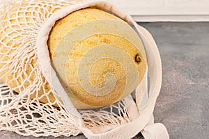 melon in a cotton net. Mesh shopping bag with Torpedo melon. Ripe juicy melon in a cotton mesh bag on a marble light