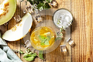 Melon lemonade in glasses with ice and mint on a wooden rustic table. Fresh refreshing fruity summer drink, seasonal beverages.