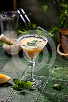Melon margarita cocktail with mint in glass on dark green ceramic tile background