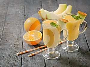 Melon, orange, cocktail tubes and melon smoothies in glass glasses on a rustic table.