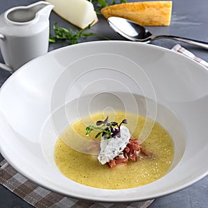 Melon soup with mint, proshuto and cucumber. White plate, tureen, spoon on the grey background. Close-up photo