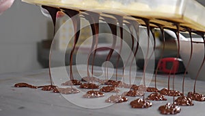 Melted chocolate dripping from tempering molds. Confectioner holding forms of handmade candies with melted chocolate