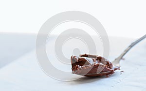Melted chocolate paste in a spoon on a whte stone background. Cl